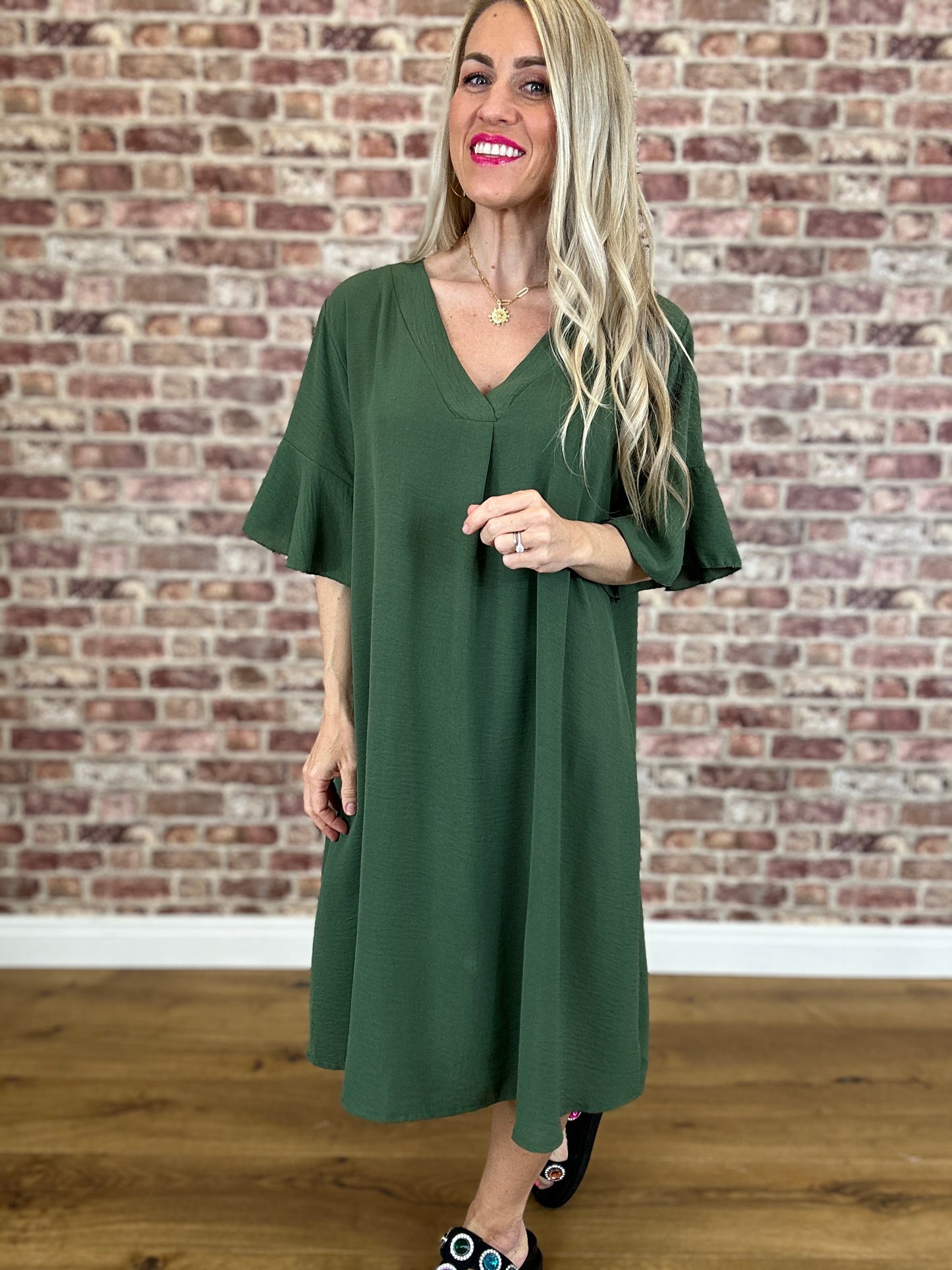 Woman wearing a green dress standing in front of a brick wall.