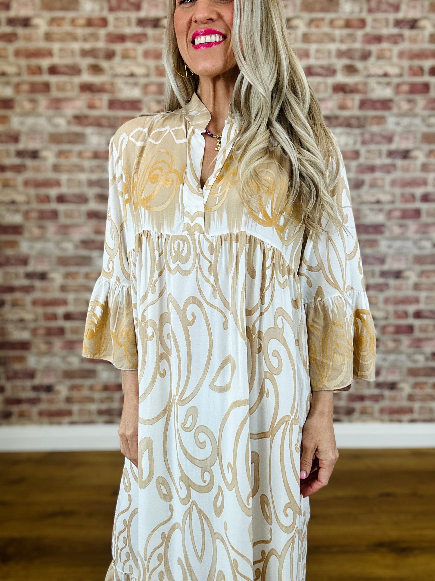 Woman wearing a patterned dress standing against a brick wall.