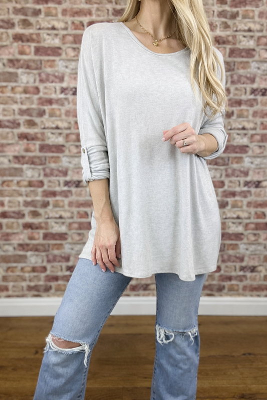 Person wearing a light gray long-sleeve top and ripped jeans against a brick wall.