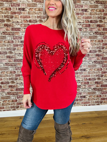 Person wearing a red sweater with a heart design in front of a brick wall.