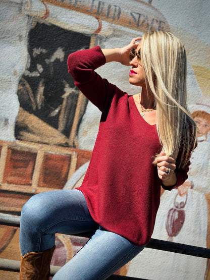 Woman in a red sweater and blue jeans sitting on a bench with a decorative wall in the background