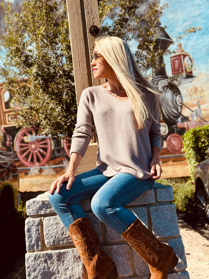 Woman sitting on stone steps wearing a beige sweater and blue jeans with brown boots, with a colorful background.