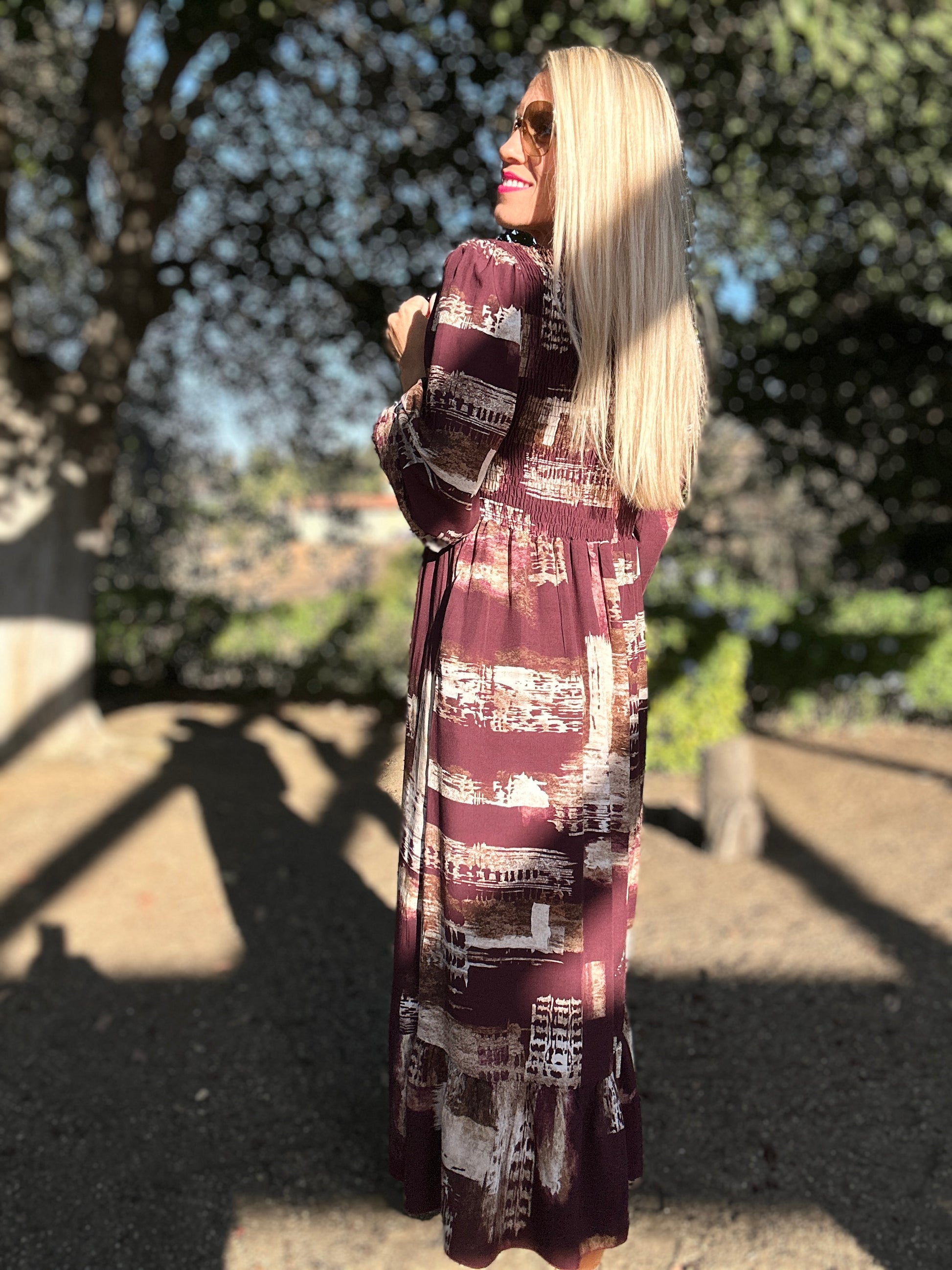 Woman wearing a long, patterned dress standing outdoors with trees in the background