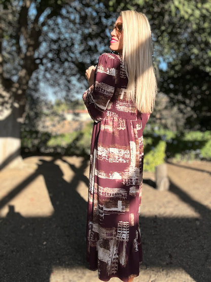 Woman wearing a long, patterned dress standing outdoors with trees in the background