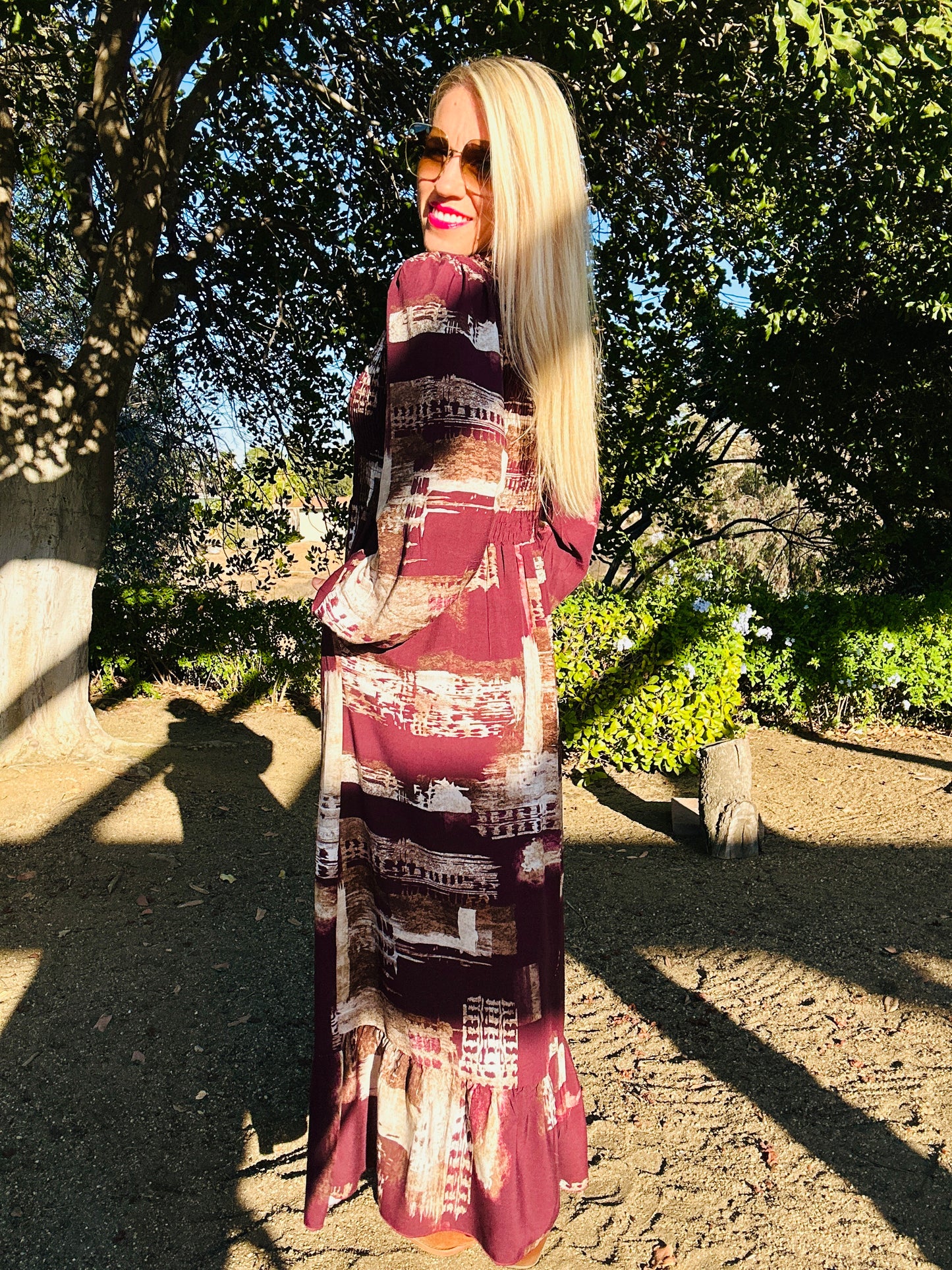 Woman wearing a patterned dress standing outdoors with trees in the background