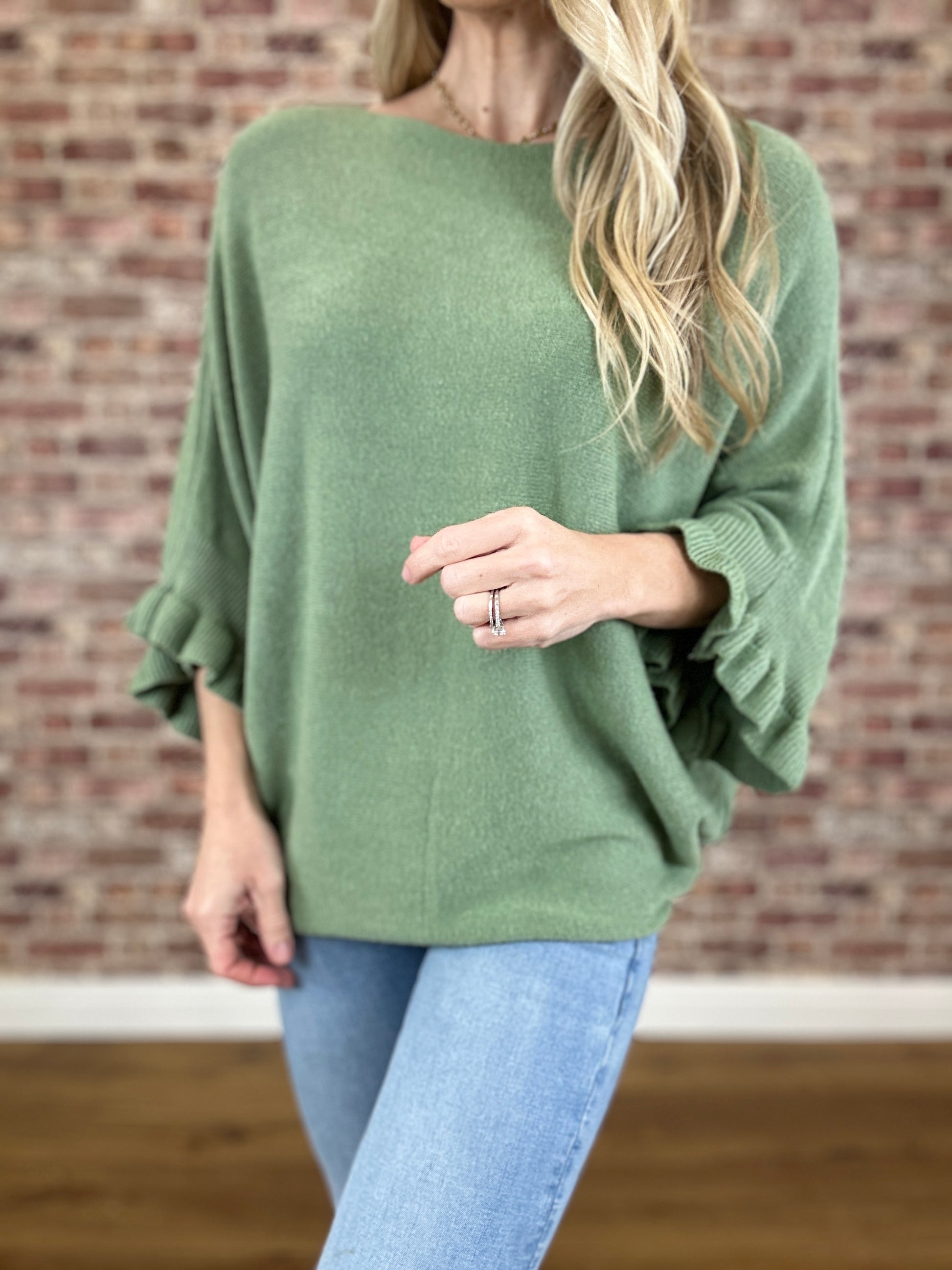 Person wearing a green sweater with ruffled sleeves against a brick wall.