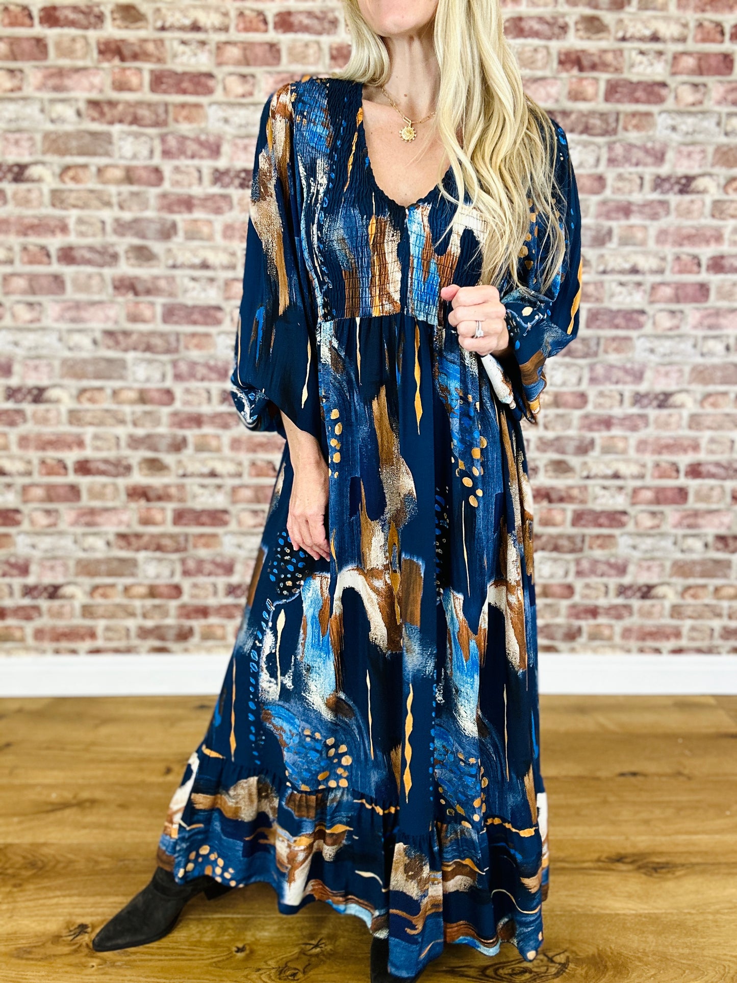 Woman wearing a long, patterned dress against a brick wall.