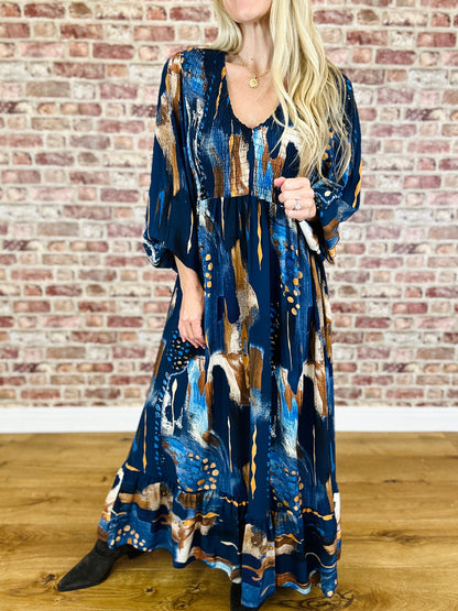 Woman wearing a long, patterned dress against a brick wall.