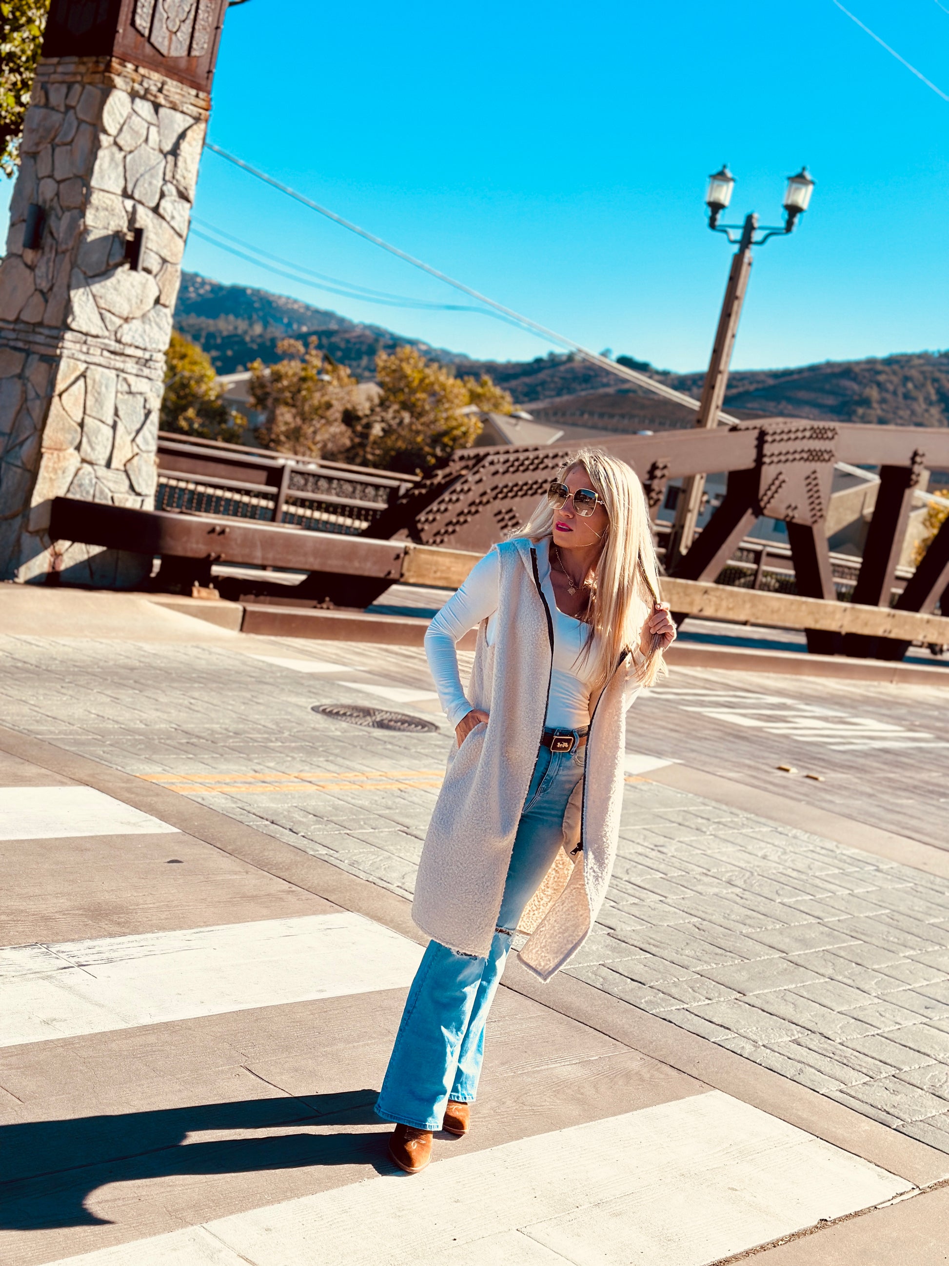 Woman in a long coat standing on a street with mountains in the background