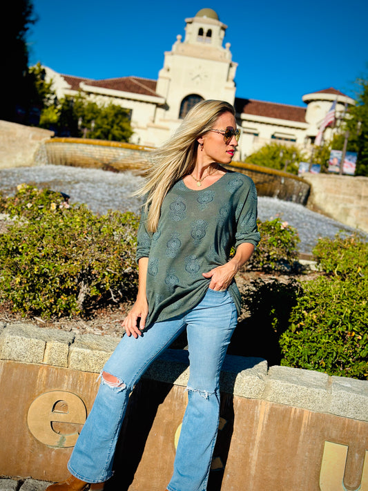 Woman in green top and blue jeans standing in front of a building with a clock tower.