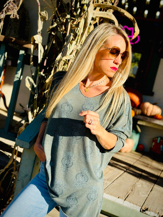 Woman wearing a gray patterned top and sunglasses outdoors with decorative elements in the background