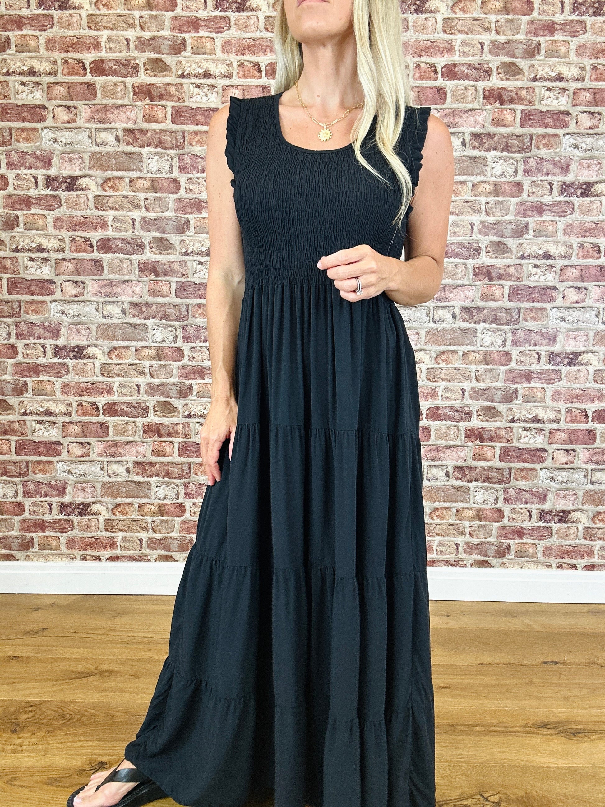Woman wearing a black sleeveless dress against a brick wall.