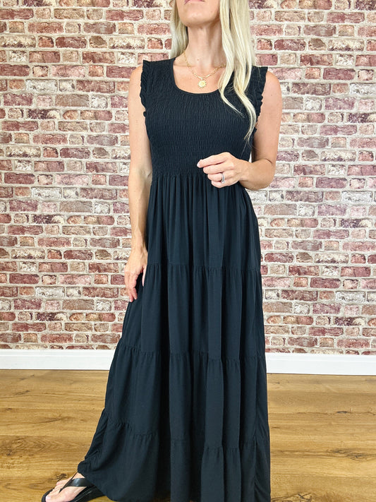 Woman wearing a black sleeveless dress against a brick wall.