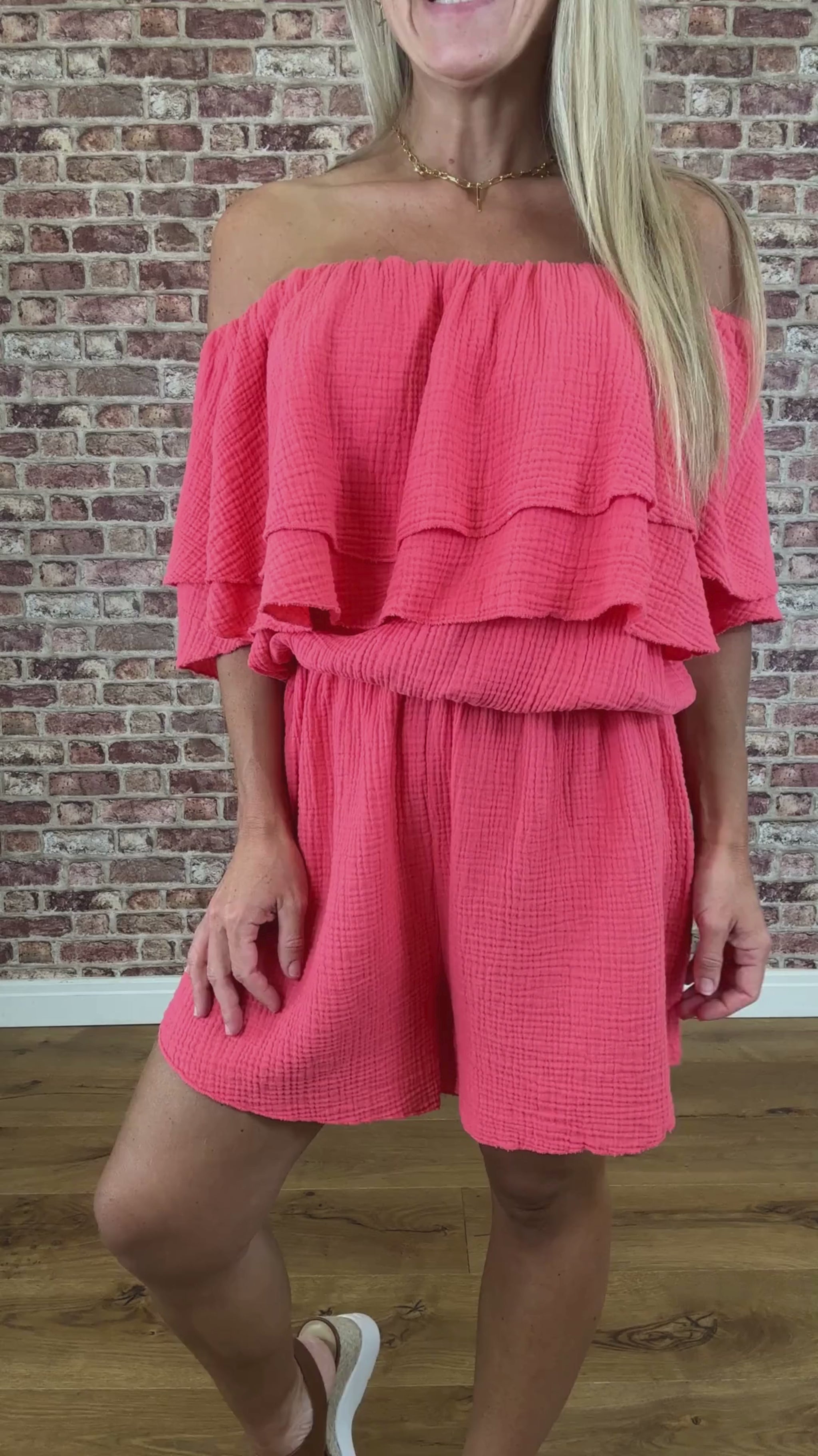 Woman wearing a coral layered dress against a brick wall.