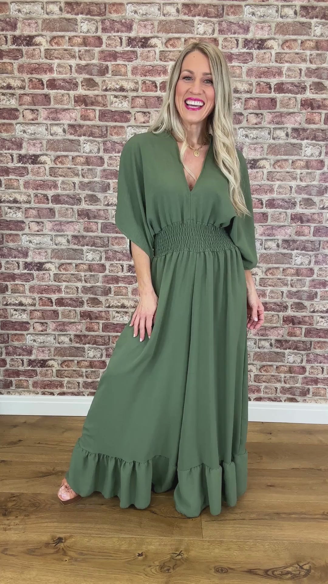 A woman wearing a green jumpsuit with a deep V-neckline, loose fit, and frill detail at the ankle.