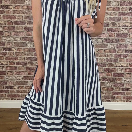 Person wearing a navy and white striped dress against a brick wall.