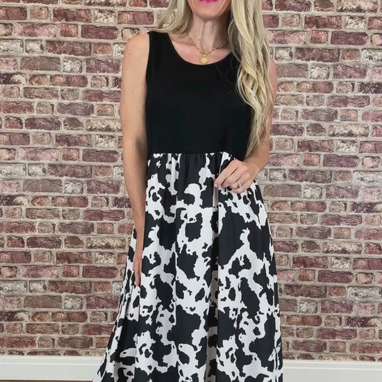 Woman wearing a black sleeveless top and cow print skirt against a brick wall.