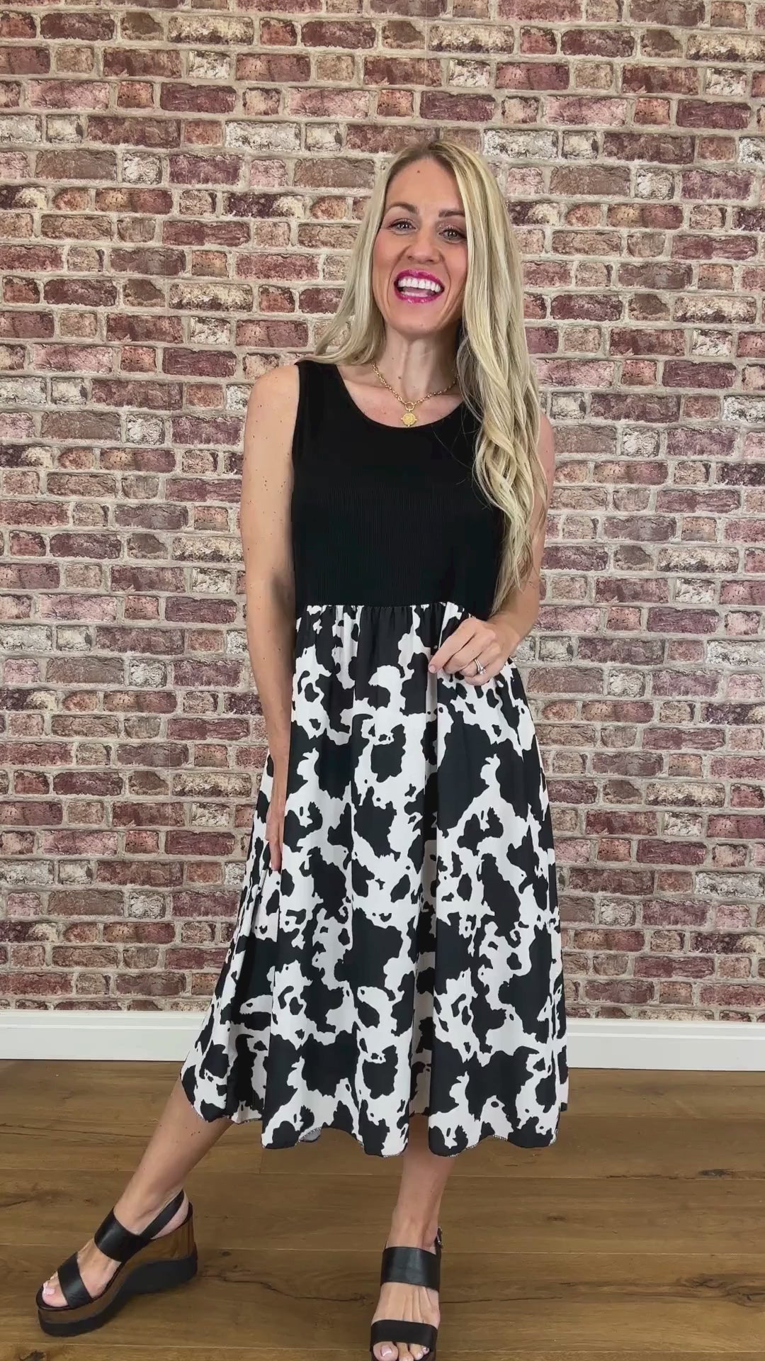Woman wearing a black sleeveless top and cow print skirt against a brick wall.