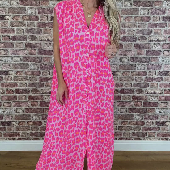 Woman wearing a pink leopard print dress standing against a brick wall.