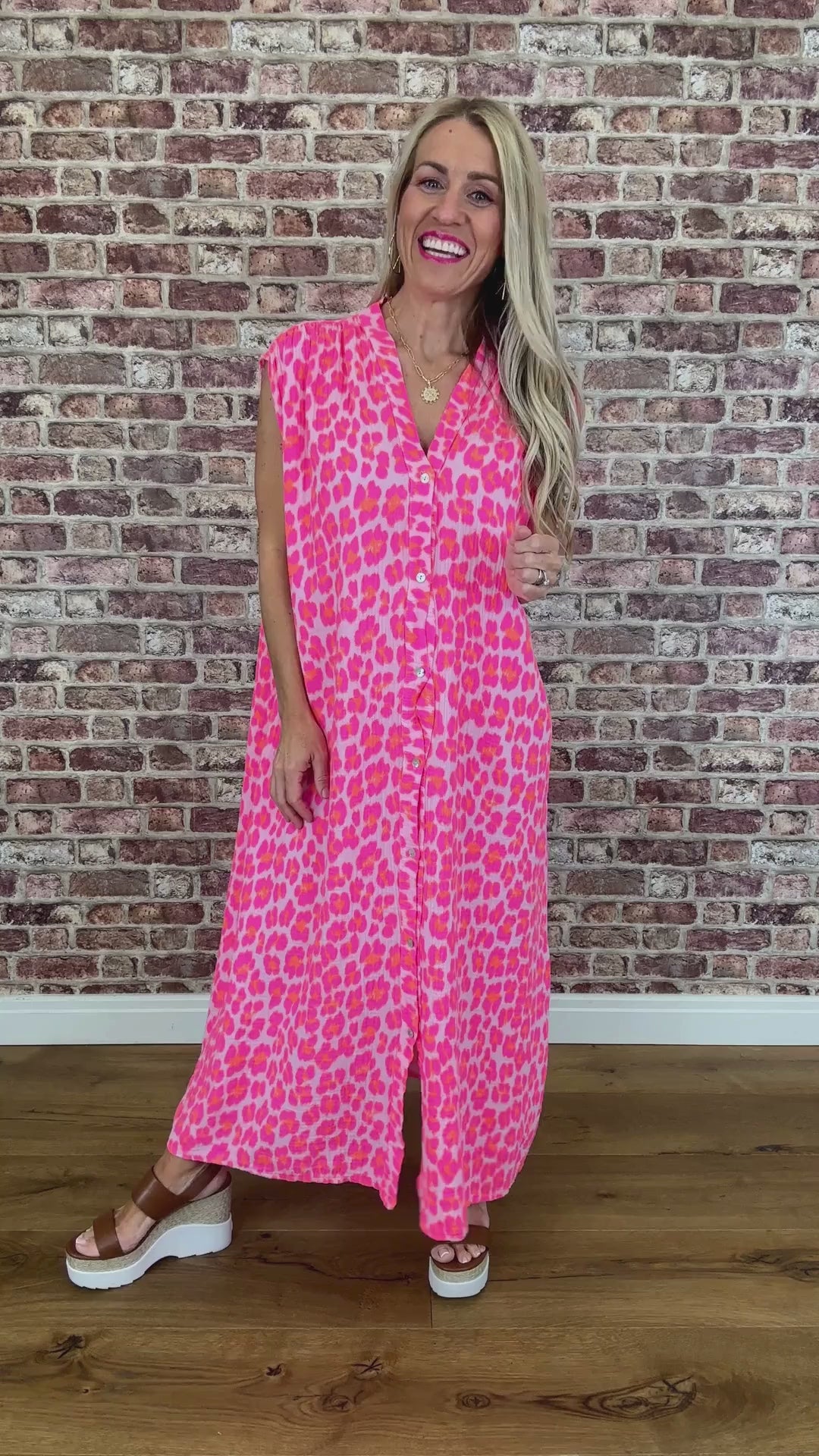Woman wearing a pink leopard print dress standing against a brick wall.
