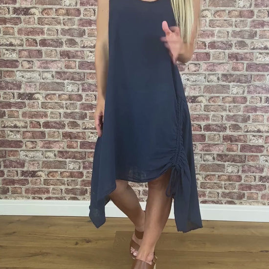 Woman wearing a navy blue dress standing against a brick wall.