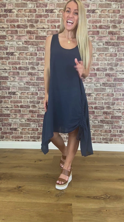 Woman wearing a navy blue dress standing against a brick wall.