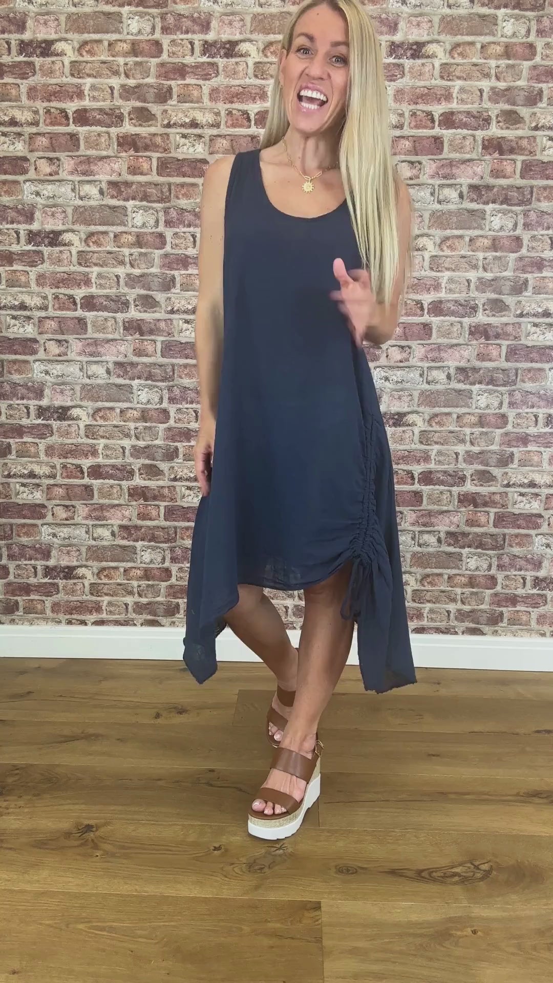 Woman wearing a navy blue dress standing against a brick wall.