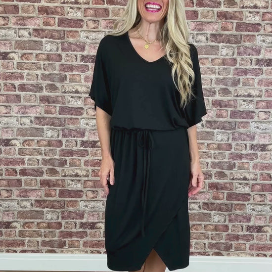 Person wearing a black dress standing against a brick wall.