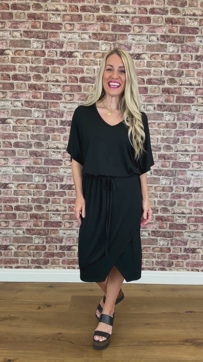 Person wearing a black dress standing against a brick wall.