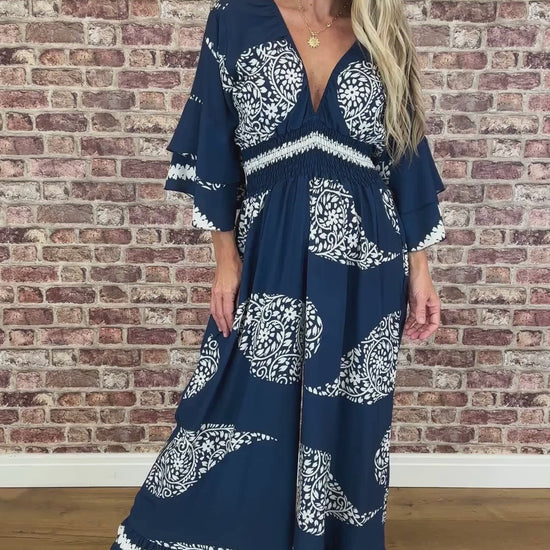 Woman wearing a blue and white patterned dress against a brick wall.