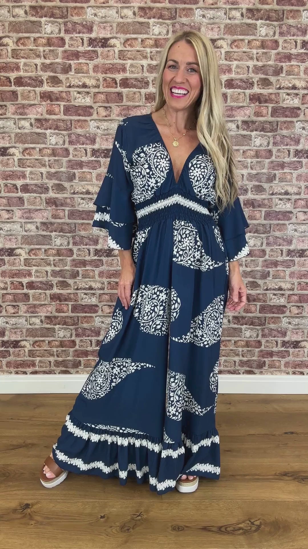 Woman wearing a blue and white patterned dress against a brick wall.