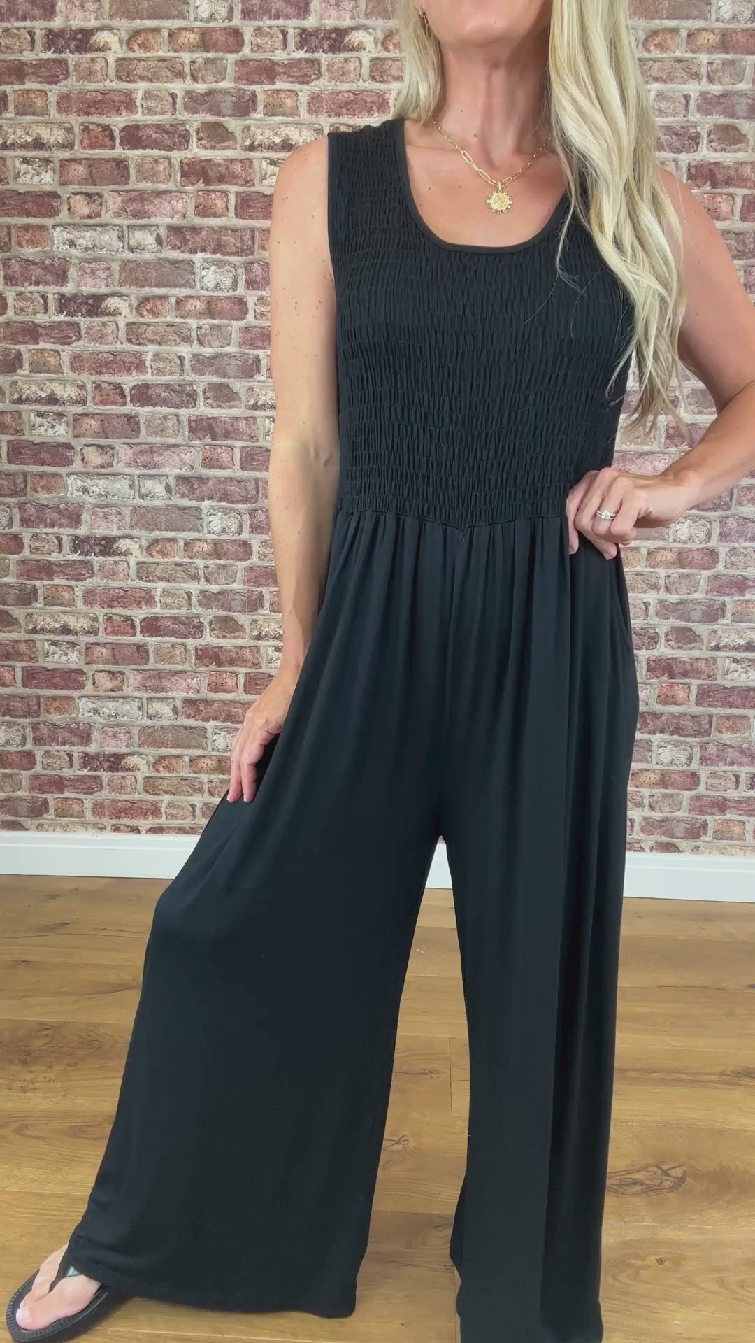 Person wearing a black jumpsuit against a brick wall.