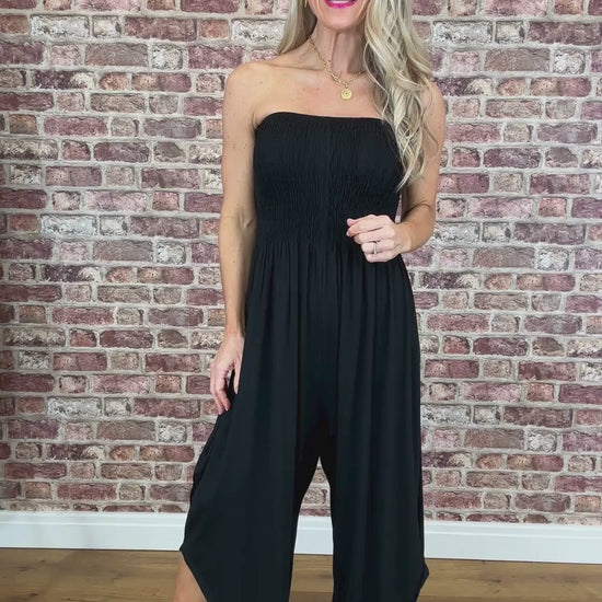 woman wearing a black strapless jumpsuit in front of a brick background