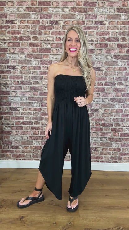 woman wearing a black strapless jumpsuit in front of a brick background