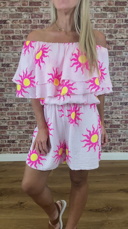 Woman wearing a pink and yellow sun-patterned dress against a brick wall.