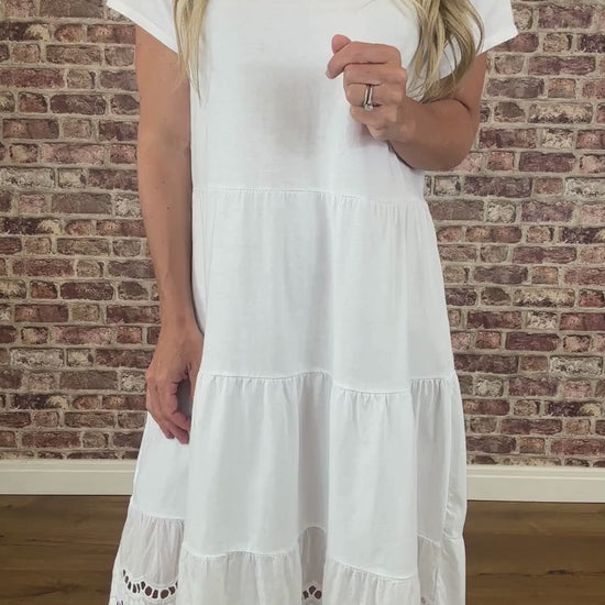 Woman wearing a white dress standing against a brick wall.