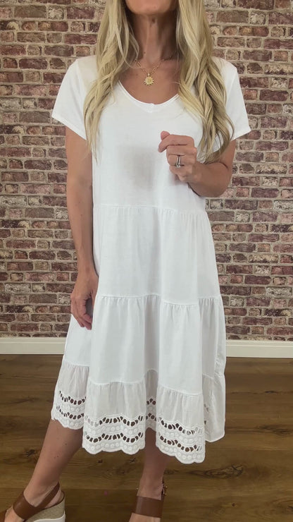 Woman wearing a white dress standing against a brick wall.