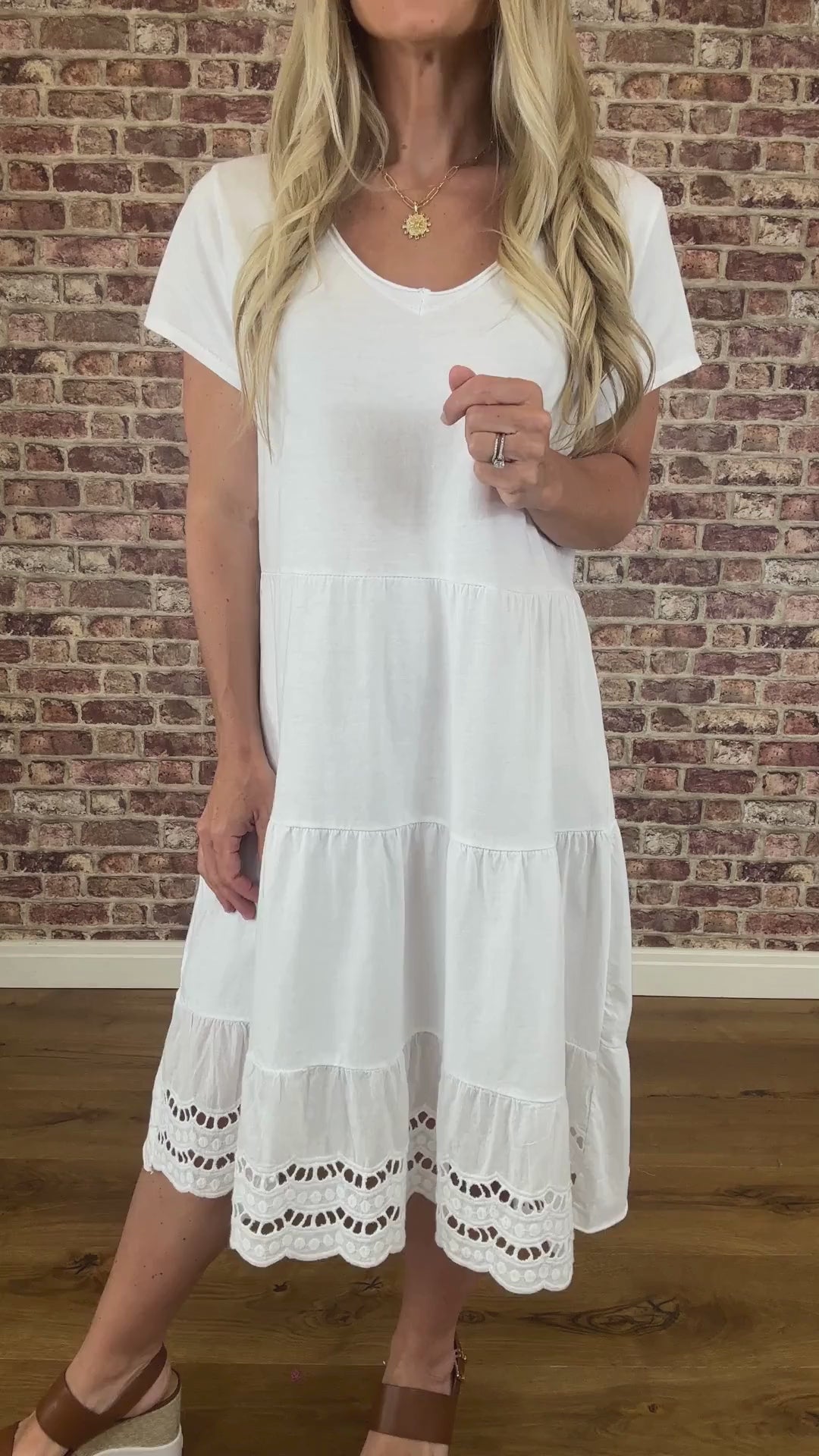 Woman wearing a white dress standing against a brick wall.