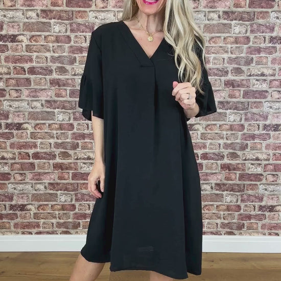 Woman wearing a black dress standing against a brick wall.