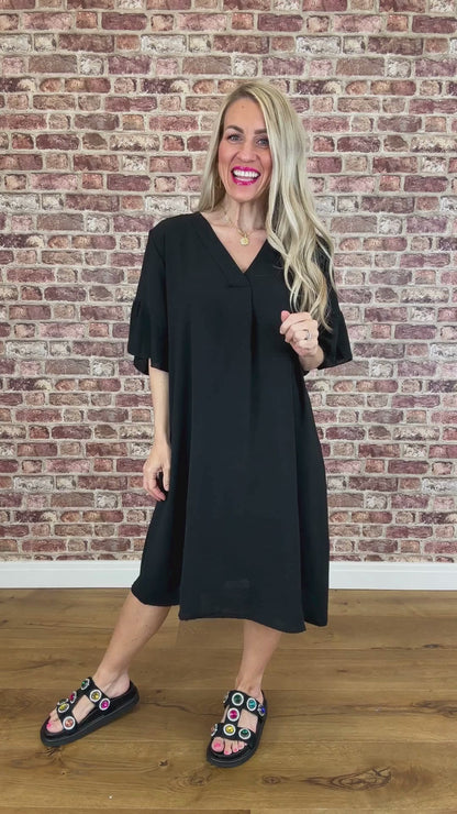 Woman wearing a black dress standing against a brick wall.