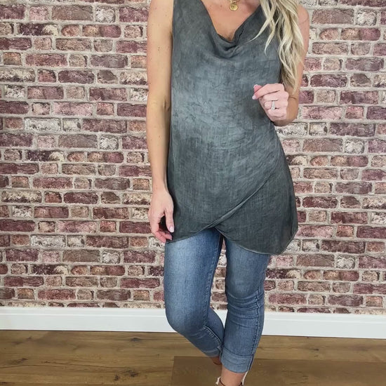 A model wearing a sleeveless gray vest with a scooping cowl neckline and light blue jeans.