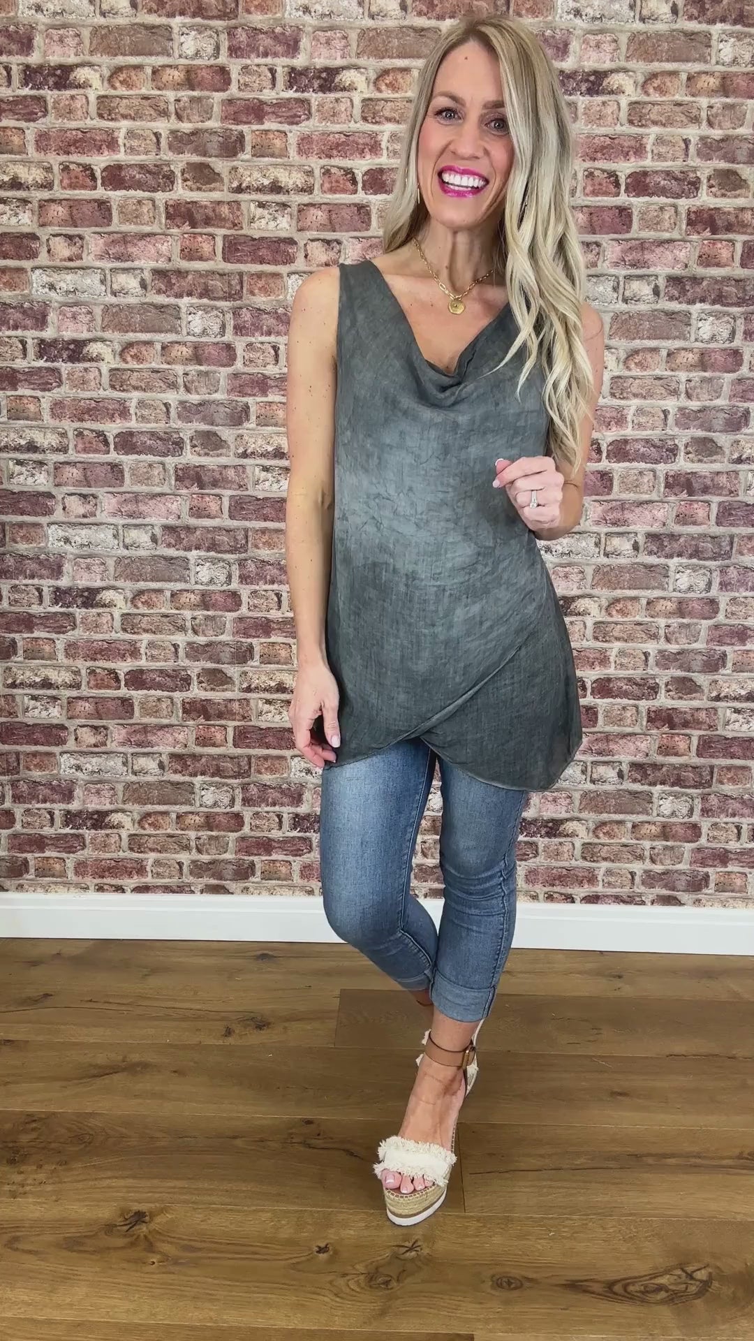 A model wearing a sleeveless gray vest with a scooping cowl neckline and light blue jeans.